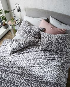 a leopard print comforter set on a bed with pink pillows and grey linens