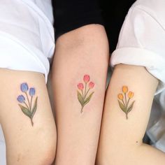 two women with matching tattoos on their legs, both have colorful flowers tattooed on them