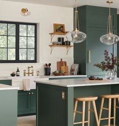 a kitchen with green cabinets and white counter tops, two hanging lights above the island