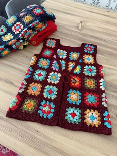 a crocheted vest sitting on top of a wooden table next to some blankets