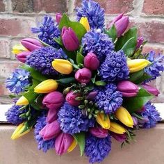 a bouquet of purple and yellow flowers in front of a brick wall