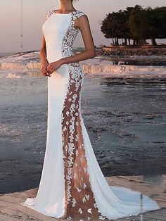 a woman in a white and brown dress standing on the beach with her back to the camera