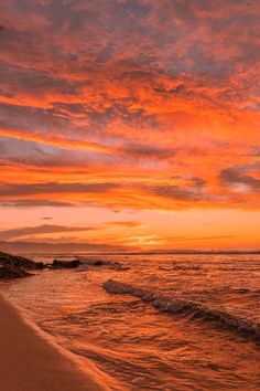 an orange and pink sunset over the ocean with waves coming in to shore on a sandy beach