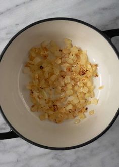 chopped onions in a white bowl on top of a marble countertop next to a black frying pan