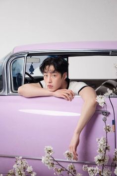 a young man leaning on the hood of a purple car with flowers growing out of it