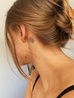 a woman with a small sun tattoo on her left side behind her ear, looking down at the ground