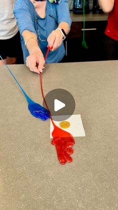 a woman is painting with red, blue and yellow paint on the counter top in front of her