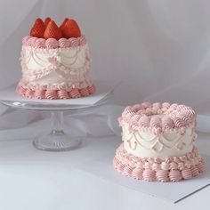 two cakes with pink frosting and strawberries on top, one is decorated in white icing