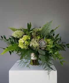 a bouquet of green flowers and greenery in a white vase on top of a table