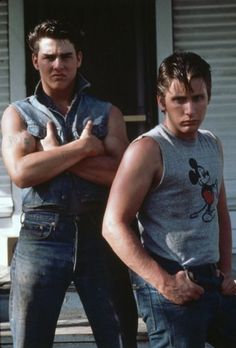 two young men standing next to each other in front of a house with their arms crossed