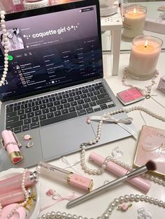 an open laptop computer sitting on top of a white table next to pearls and candles