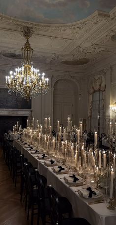 a long table with many candles on it in a fancy dining room, surrounded by chandeliers