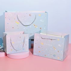 three paper bags with necklaces on them sitting on a pink table next to other items