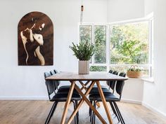 a dining room table with chairs and a painting on the wall in front of it