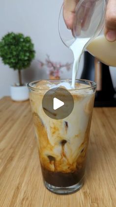 a person pouring milk into a glass on top of a wooden table