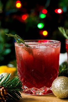 two glasses filled with red liquid and garnished with rosemary, sitting on a table next to christmas decorations