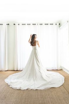 a woman standing in front of a window wearing a wedding dress