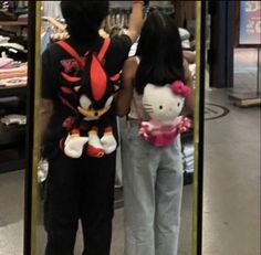 two people standing in front of a mirror with hello kitty stuffed animal on it's back