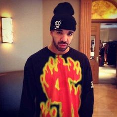 a man wearing a black hat and shirt with flames on it is standing in a hallway