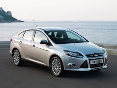 a silver car is parked on the side of the road near the water and rocks