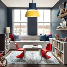 a child's room with blue walls and red chairs, a white table, bookshelves and a yellow lamp