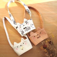 three small purses with cats on them sitting on a table next to dried flowers