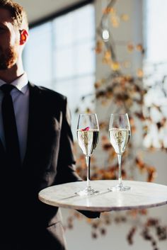 a man in a suit holding a tray with two glasses of wine on it,