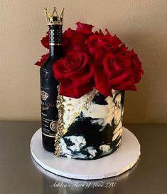 a black and white cake with red roses on top, next to a bottle of wine