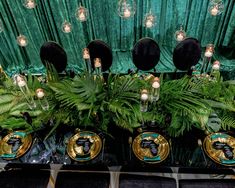 a table topped with plates covered in green plants and gold rimmed dishes filled with candles