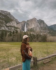 a woman standing in front of a mountain with a waterfall coming out of the distance