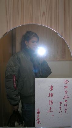 a man standing in front of a mirror holding a light up to his face with chinese writing on it