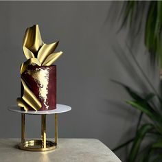 a red and gold cake sitting on top of a white plate next to a potted plant