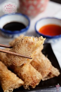 some food is on a black plate with chopsticks and sauce in the background