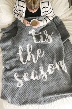 a woman sitting on top of a bed covered in a blanket and holding a cup