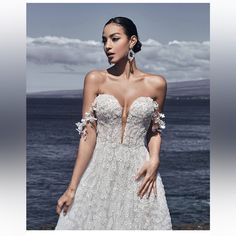 a woman in a wedding dress standing by the ocean with her hands on her hips