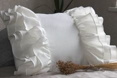 a white pillow with ruffled edges and a bundle of dried flowers on the bed