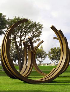 an abstract sculpture in the middle of a grassy area with trees and grass behind it