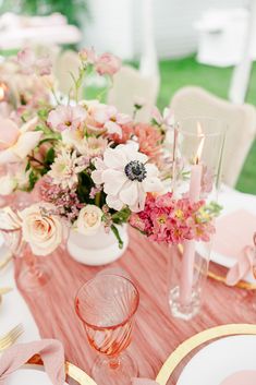 the table is set with pink and white flowers in vases, candles, and napkins