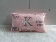 a pink pillow with the letter k on it sitting on a white furnishing