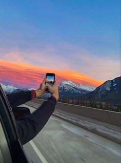 a man taking a photo with his cell phone while driving down the highway at sunset