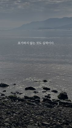 the words are written in korean on rocks near the water's edge with mountains in the background