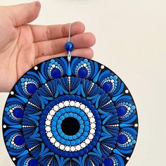 a hand holding a blue and white circular ornament on a white surface with beads