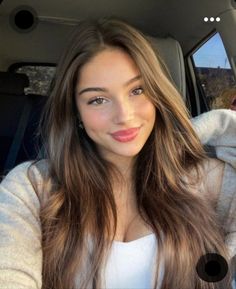 a woman sitting in the back seat of a car with long brown hair and blue eyes