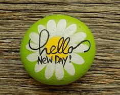 a green and white painted rock with the words hello new day on it sitting on a wooden surface