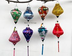 a bunch of different colored lanterns hanging from a tree branch in front of a white wall