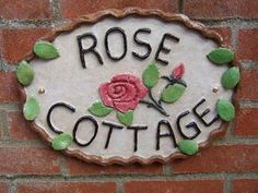 a sign that says rose cottage on the side of a brick wall