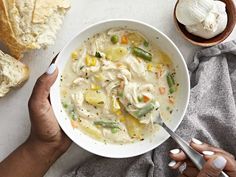 two hands holding a bowl of chicken noodle soup next to a loaf of bread