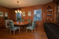 a dining room with wood paneling and blue chairs around a wooden table in front of a window