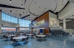 an empty cafeteria with tables and chairs in the center, looking towards the front door