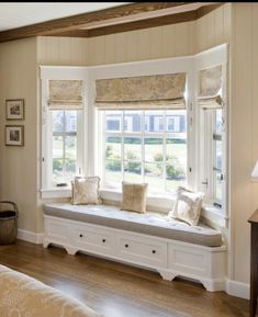 a window seat in the corner of a room with two windows and pillows on it